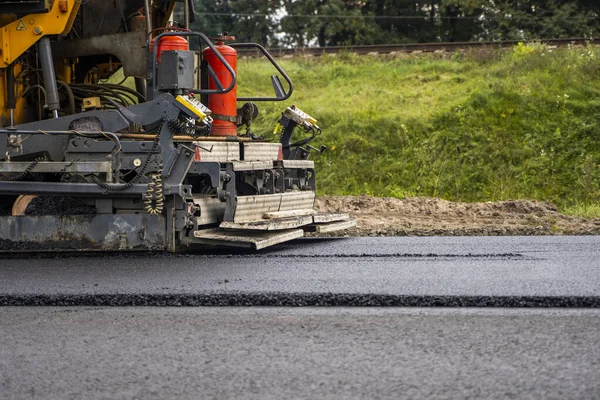 Industriell asfaltläggare maskin som lägger färsk asfalt på väg byggarbetsplats. — Stockfoto