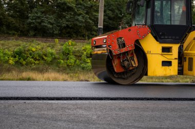 Ağır titreşimli paten sıkıştırıcılı asfalt yol silindiri bir yol inşaatındaki yolda yeni bir sıcak asfalta bastırıyor. Asfalt kaldırımda ağır titreşimli silindir çalışıyor. Onarılıyor.
