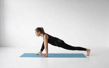 Genç bir kadın stüdyoda yoga yapıyor. Siyah spor giysili zayıf genç kız mavi bir minderde yoga çalışması yapıyor. Vücut ve zihinsel gelişim arasındaki sağlıklı yaşam ve doğal denge kavramı.