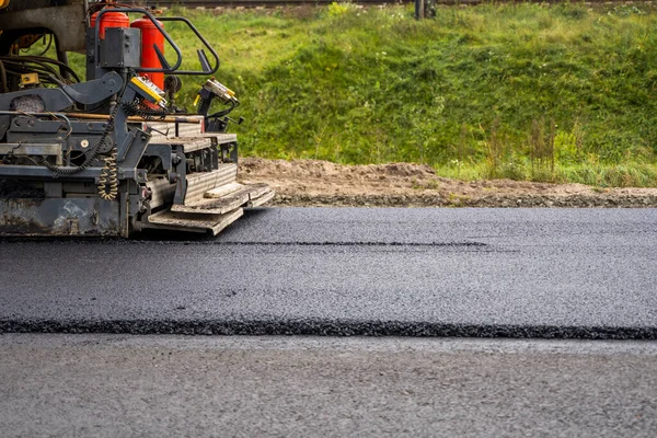 Industriell asfaltläggare maskin som lägger färsk asfalt på väg byggarbetsplats. — Stockfoto