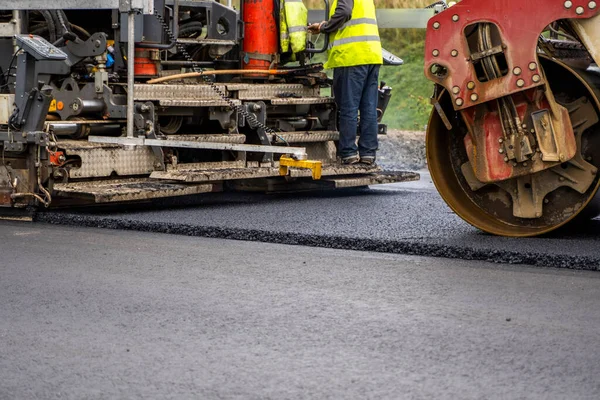 Industriell asfaltläggare maskin som lägger färsk asfalt på väg byggarbetsplats. — Stockfoto