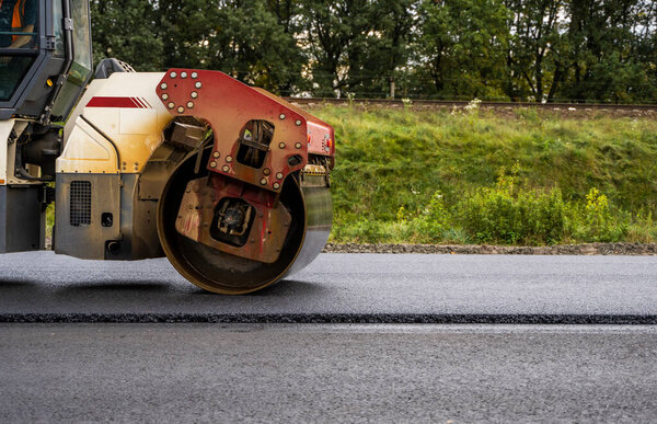 Asphalt road roller with heavy vibration roller compactor press new hot asphalt on the roadway on a road construction site. Heavy Vibration roller at asphalt pavement working. Repairing.