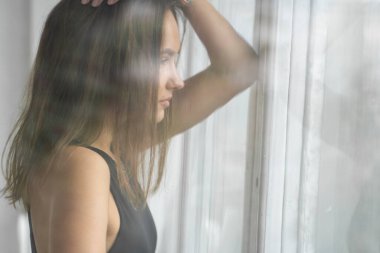 Beyaz bir stüdyoda açık bir pencerenin arkasında siyah iç çamaşırı ve mavi kot pantolon giymiş genç, dalgın esmer kadın portresi. Temel giysili güzel bir kız için model testleri.