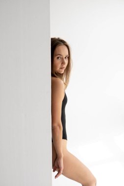 Genç, esmer, sıska bir kadının portresi siyah iç çamaşırlarıyla beyaz bir stüdyoda beyaz bir duvarın arkasında poz veriyor. Güzel bir kızın temel kıyafetlerini siklonamada test etmek..