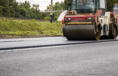 Ağır titreşimli paten sıkıştırıcılı asfalt yol silindiri bir yol inşaatındaki yolda yeni bir sıcak asfalta bastırıyor. Asfalt kaldırımda ağır titreşimli silindir çalışıyor. Onarılıyor.