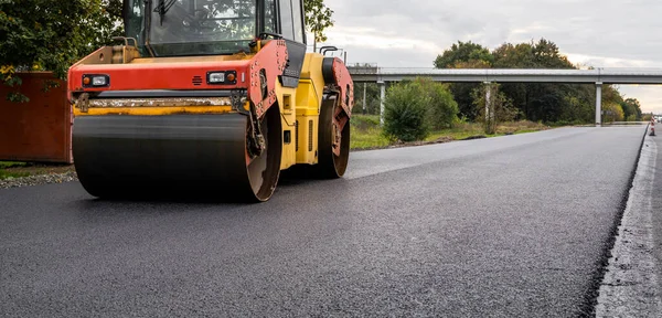 Ağır titreşimli paten sıkıştırıcılı asfalt yol silindiri bir yol inşaatındaki yolda yeni bir sıcak asfalta bastırıyor. Asfalt kaldırımda ağır titreşimli silindir çalışıyor. Onarılıyor.