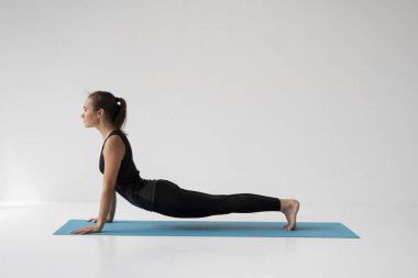Yoga yapan, yalan söyleyen ve Kobra pozu veren genç bir kadın Bhujangasana egzersizi yapıyor. Siyah spor giyimli çekici bir kız. Güzel, formda bir yogacı kadın yoga yapıyor, asana bhujangasana.