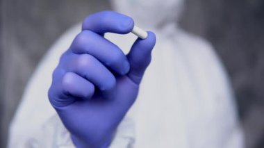 Beyaz koruyucu giysili, tıbbi maskeli ve lastik eldivenli doktor beyaz hapları koronavirüs salgınına karşı bir tehdit olarak tutuyor. Salgın, Coronavirus covid 19 salgını..