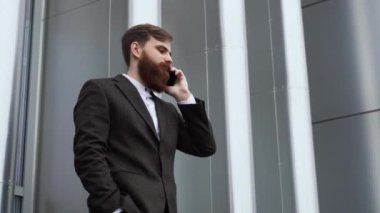 Finans bölgesinde iş adamı telefonda konuşuyor. Ofis binasının üzerinde akıllı telefon kullanan genç bir şehirli adamın portresi. İş adamı dışarıda akıllı telefonuyla konuşuyor. Teknoloji.