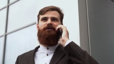 Finans bölgesinde iş adamı telefonda konuşuyor. Ofis binasının üzerinde akıllı telefon kullanan genç bir şehirli adamın portresi. İş adamı dışarıda akıllı telefonuyla konuşuyor. Teknoloji.