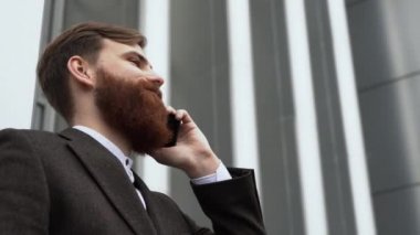 Finans bölgesinde iş adamı telefonda konuşuyor. Ofis binasının üzerinde akıllı telefon kullanan genç bir şehirli adamın portresi. İş adamı dışarıda akıllı telefonuyla konuşuyor. Teknoloji.
