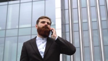 Finans bölgesinde iş adamı telefonda konuşuyor. Ofis binasının üzerinde akıllı telefon kullanan genç bir şehirli adamın portresi. İş adamı dışarıda akıllı telefonuyla konuşuyor. Teknoloji.