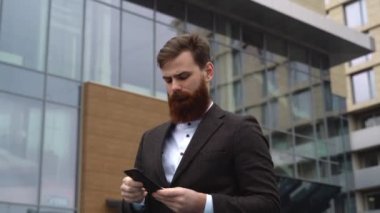 Finans bölgesinde iş adamı telefonda konuşuyor. Ofis binasının üzerinde akıllı telefon kullanan genç bir şehirli adamın portresi. İş adamı dışarıda akıllı telefonuyla konuşuyor. Teknoloji.