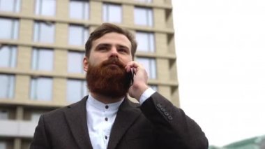 Finans bölgesinde iş adamı telefonda konuşuyor. Ofis binasının üzerinde akıllı telefon kullanan genç bir şehirli adamın portresi. İş adamı dışarıda akıllı telefonuyla konuşuyor. Teknoloji.