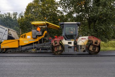 KYIV, UKRAINE - 25 Eylül 2020: İki ağır asfalt yol silindiri ve ağır titreşimli paten sıkıştırıcısı bir cadde üzerindeki yol inşaatında yeni bir sıcak asfalta baskı yapıyor..