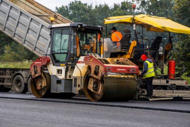KYIV, UKRAINE - 25 Eylül 2020::: Ağır titreşimli asfalt yol silindiri, yeni asfalt ve asfalt kaldırım taşıma makinesine baskı yapan ağır titreşimli paten sıkıştırıcısı.