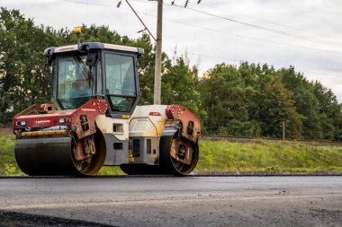 KYIV, UKRAINE - 25 Eylül 2020: Ağır sarı asfalt yol silindirli ağır titreşimli paten sıkıştırıcı bir caddedeki yol inşaatında yeni bir sıcak asfalta basıyor.