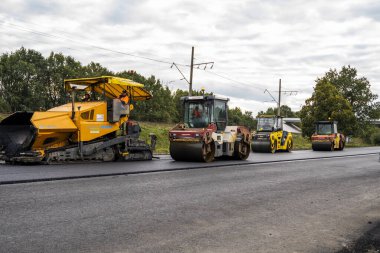 KYIV, UKRAINE - 25 Eylül 2020::: Ağır titreşimli asfalt yol silindiri, yeni asfalt ve asfalt kaldırım taşıma makinesine baskı yapan ağır titreşimli paten sıkıştırıcısı.