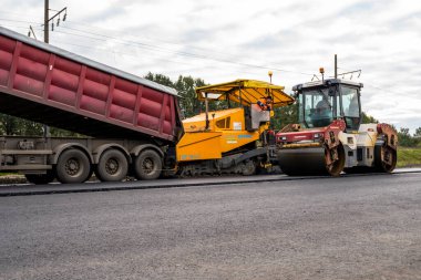 KYIV, UKRAINE - 25 Eylül 2020::: Ağır titreşimli asfalt yol silindiri, yeni asfalt ve asfalt kaldırım taşıma makinesine baskı yapan ağır titreşimli paten sıkıştırıcısı.