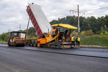 KYIV, UKRAINE - 25 Eylül 2020::: Ağır titreşimli asfalt yol silindiri, yeni asfalt ve asfalt kaldırım taşıma makinesine baskı yapan ağır titreşimli paten sıkıştırıcısı.