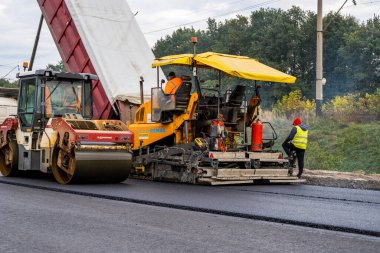 KYIV, UKRAINE - 25 Eylül 2020::: Ağır titreşimli asfalt yol silindiri, yeni asfalt ve asfalt kaldırım taşıma makinesine baskı yapan ağır titreşimli paten sıkıştırıcısı.