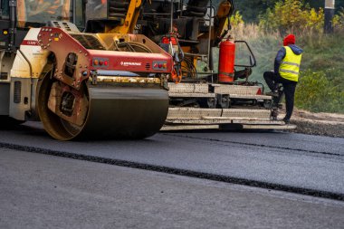 KYIV, UKRAINE - 25 Eylül 2020::: Ağır titreşimli asfalt yol silindiri, yeni asfalt ve asfalt kaldırım taşıma makinesine baskı yapan ağır titreşimli paten sıkıştırıcısı.