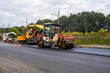 KYIV, UKRAINE - 25 Eylül 2020::: Ağır titreşimli asfalt yol silindiri, yeni asfalt ve asfalt kaldırım taşıma makinesine baskı yapan ağır titreşimli paten sıkıştırıcısı.