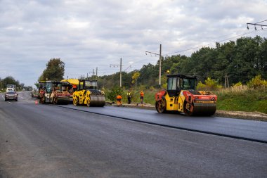 KYIV, UKRAINE - 25 Eylül 2020: İki ağır asfalt yol silindiri ve ağır titreşimli paten sıkıştırıcısı bir cadde üzerindeki yol inşaatında yeni bir sıcak asfalta baskı yapıyor..