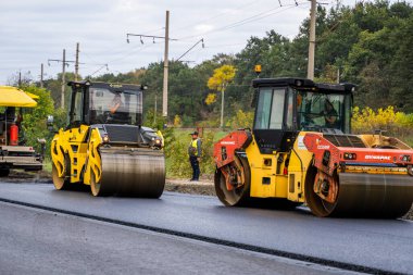 KYIV, UKRAINE - 25 Eylül 2020: İki ağır asfalt yol silindiri ve ağır titreşimli paten sıkıştırıcısı bir cadde üzerindeki yol inşaatında yeni bir sıcak asfalta baskı yapıyor..