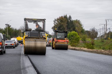 KYIV, UKRAINE - 25 Eylül 2020: İki ağır asfalt yol silindiri ve ağır titreşimli paten sıkıştırıcısı bir cadde üzerindeki yol inşaatında yeni bir sıcak asfalta baskı yapıyor..