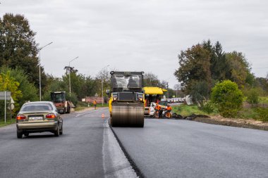 KYIV, UKRAINE - 25 Eylül 2020: Ağır sarı asfalt yol silindirli ağır titreşimli paten sıkıştırıcı bir caddedeki yol inşaatında yeni bir sıcak asfalta basıyor.