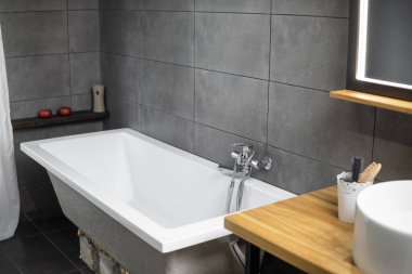 Bathroom in a concrete style with a bath, sink and big mirror.