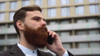 Finans bölgesinde iş adamı telefonda konuşuyor. Ofis binasının üzerinde akıllı telefon kullanan genç bir şehirli adamın portresi. İş adamı dışarıda akıllı telefonuyla konuşuyor. Teknoloji.