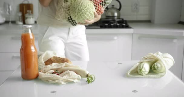 Kvinnor med en återanvändbar matsäck med grönsaker på ett vitt rent kök hemma efter matinköp. Noll avfall och plast gratis koncept. Mesh bomull shoppare med grönsaker. Ekologi. — Stockvideo