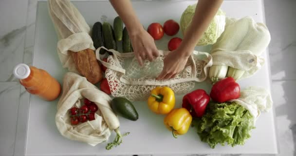 Mujer poner una col dentro de la bolsa de comestibles reutilizables con verduras en una mesa con pimientos, tomates y pepinos en la cocina. Residuos cero, plástico gratis, compras de comestibles. Comprador de algodón de malla. — Vídeos de Stock