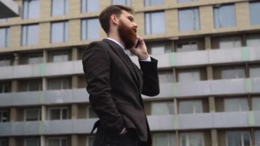 Finans bölgesinde iş adamı telefonda konuşuyor. Ofis binasının üzerinde akıllı telefon kullanan genç bir şehirli adamın portresi. İş adamı dışarıda akıllı telefonuyla konuşuyor. Teknoloji.