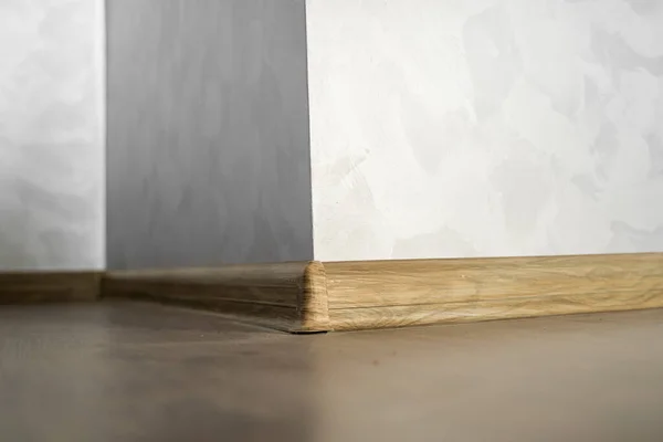 Laminado com rodapé de plástico com textura de madeira. Recém-instalado piso laminado de madeira e rodapés em casa. Design moderno. Close-up de plintos de plástico em parquet piso de carvalho de madeira escura. — Fotografia de Stock