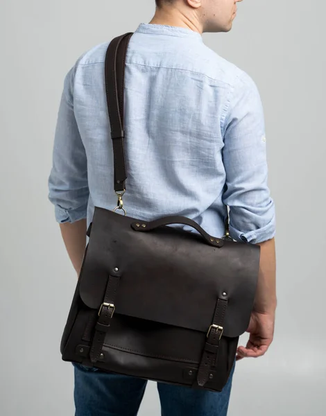 Brown mens bolsa de couro ombro para um documento e laptop sobre os ombros de um homem em uma camisa azul e jeans com um fundo branco. Satchel, mens pasta de couro artesanal. — Fotografia de Stock