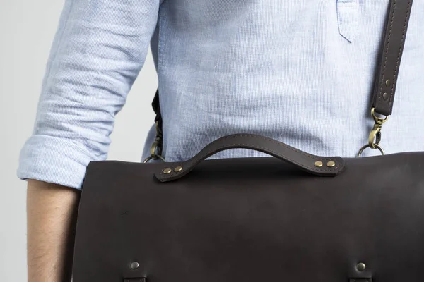 Detalles de bolso de cuero marrón para hombre para documentos y portátil en los hombros de un hombre con una camisa azul y jeans con un fondo blanco. Satchel, maletín hecho a mano de cuero para hombre. — Foto de Stock