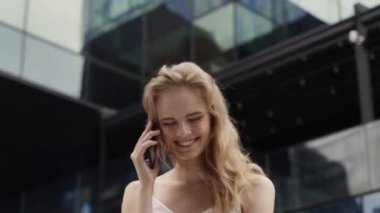 Beyaz tişörtlü genç iş kadını gülüyor ve telefonda iş ortaklarıyla konuşuyor ya da iş merkezi ya da alışveriş merkezi arkasında arkadaşlarıyla. Mutlu kız komik bir şey söyler ya da duyar..