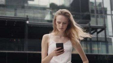 Beyaz tişörtlü genç iş kadını telefon kullanıyor ve iş ortağına ya da iş merkezine ya da alışveriş merkezine sahip arkadaşlarına mesaj yazıyor. Mutlu kız komik bir şey söyler ya da duyar..