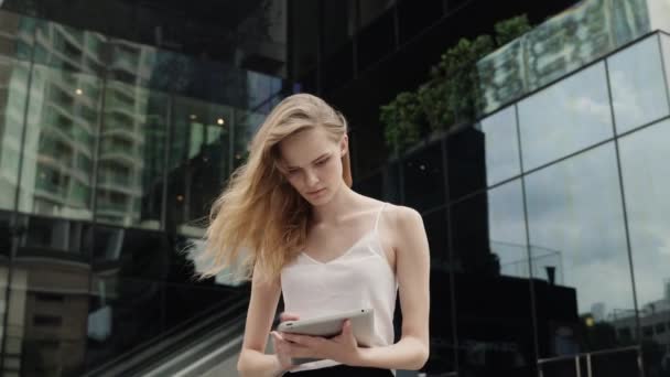 Πορτρέτο της επιχειρηματία σε ένα λευκό t-shirt χρησιμοποιεί έναν υπολογιστή tablet με ένα επιχειρηματικό κέντρο πίσω, εξωτερική. Επιχειρηματίας σε μια συνάντηση και περιμένει επιχειρηματικό εταίρο και κρατώντας ένα δισκίο στα χέρια. — Αρχείο Βίντεο