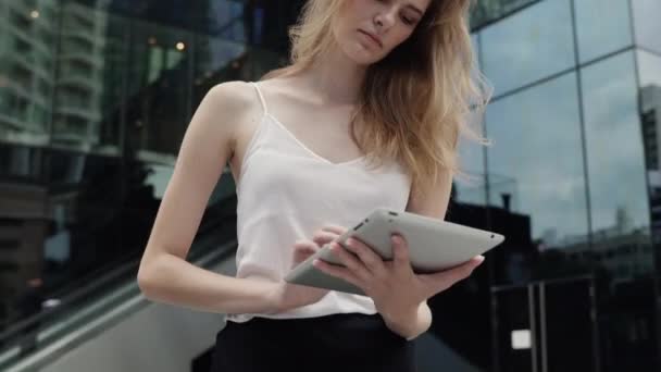 Portret bizneswoman w białej koszulce używa tabletu z centrum biznesowym za, na zewnątrz. Bizneswoman na spotkaniu i oczekiwania partnera biznesowego i trzymanie tabletu w rękach. — Wideo stockowe