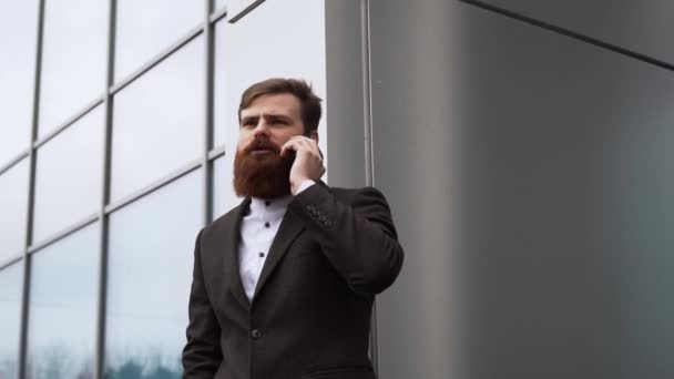 Empresário a falar ao telefone no distrito financeiro. Retrato de um jovem profissional urbano usando telefone inteligente sobre prédio de escritórios. Homem de negócios falando em seu smartphone ao ar livre. Tecnologia. — Vídeo de Stock