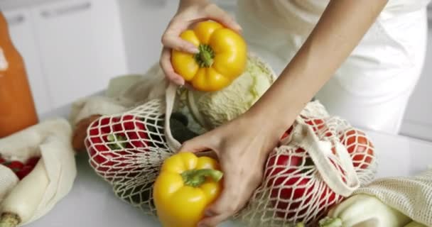 Woman takes yellow and red pepper out from reusable grocery bag with vegetables on a table at the kitchen at home after grocery shopping. Zero waste and plastic free concept. Mesh cotton shopper. — Stock Video