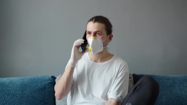 白いTシャツと医療用マスクの男は、マスクは、電話で友人やパートナーと話しています。コロナウイルスのパンデミック。家にいて、 COVID-19 、隔離. — ストック動画