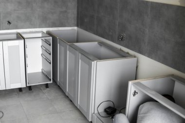 Mobilya cepheli mutfak dolapları döşemesi. Gri modüler mutfak, çeşitli kurulum aşamalarındaki çip malzemelerinden. Bir çerçeve mobilya MDF profilinin önünde.