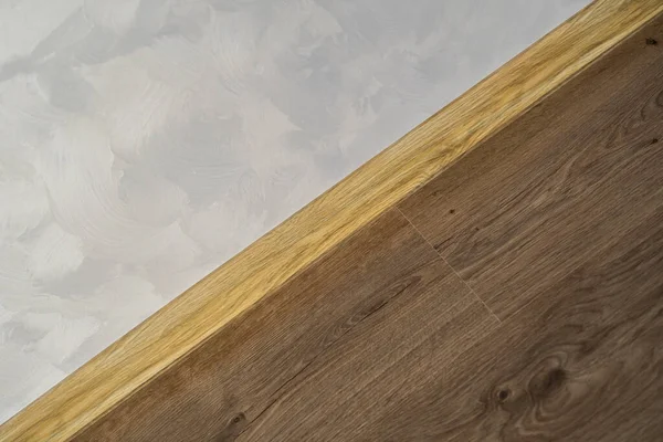 Ламінат з пластиковим плінтусом з дерев'яною текстурою. Нещодавно встановлені дерев'яні ламіновані підлоги і плити в домашніх умовах. Сучасний дизайн. Крупним планом пластикові плінтуси на темному дерев'яному паркеті з дубової підлоги . — стокове фото
