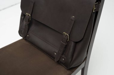 Kahverengi erkek omuz deri çantasının ayrıntıları bir belge ve beyaz arka planı olan kahverengi bir sandalyede dizüstü bilgisayar için. Erkek deri çanta, kurye çantası, deri çanta, el yapımı çanta..