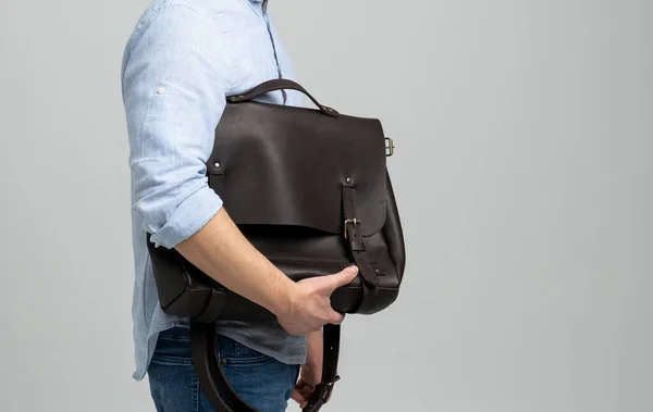 Sac bandoulière en cuir pour homme marron pour documents et ordinateur portable sur les épaules d'un homme en chemise bleue et jean à fond blanc. Cartable, mallette en cuir pour homme. — Photo